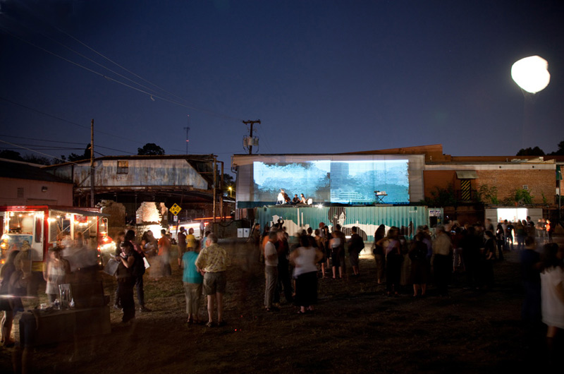 Wide shot of the event, showing 2 large projections, 3 storage containers, and the crowd